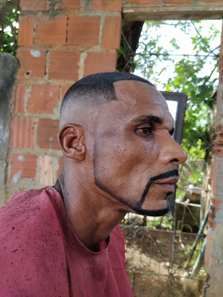 a man with black paint on his face sitting in front of a brick wall and looking off into the distance