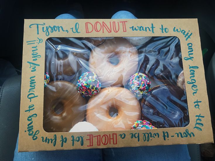 a person holding up a box full of donuts with frosting and sprinkles