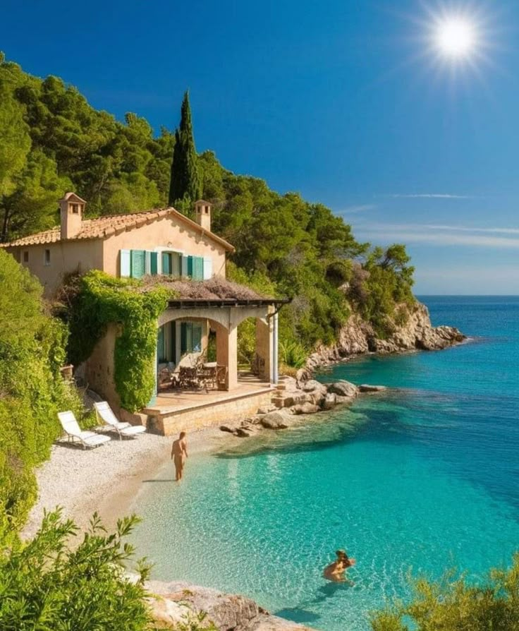 people are swimming in the clear blue water near a house on a cliff overlooking the ocean