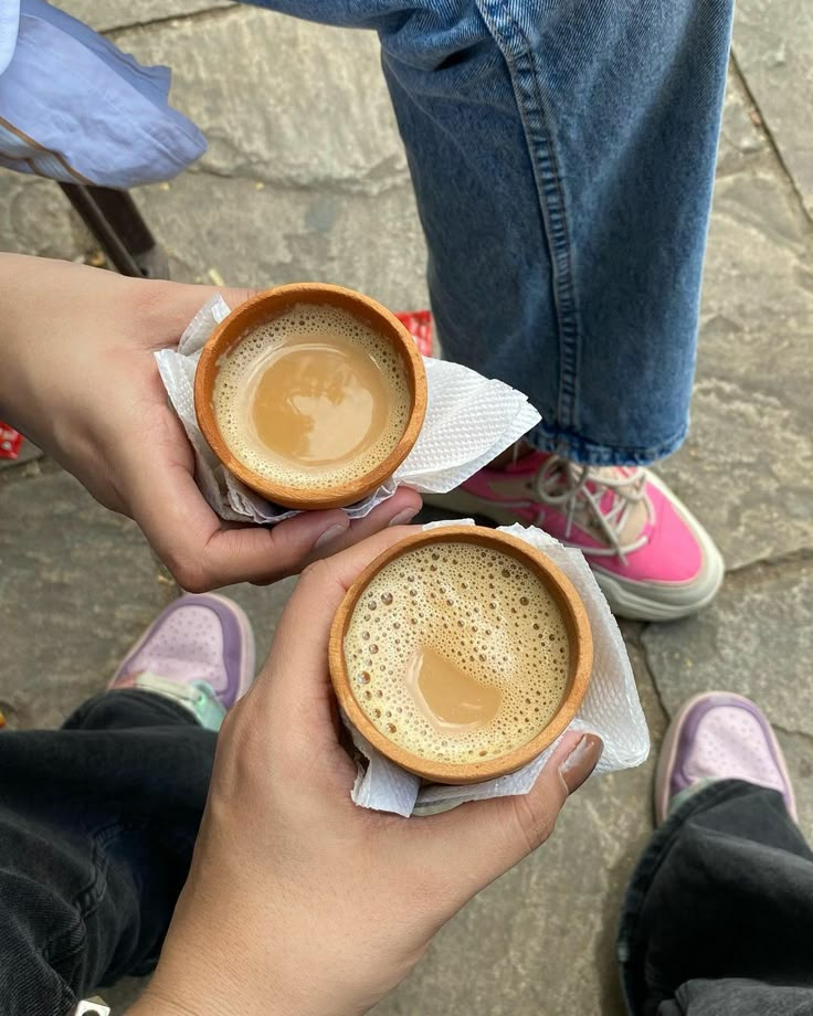 two people holding cups of coffee on top of napkins in their hands, with one person's legs crossed