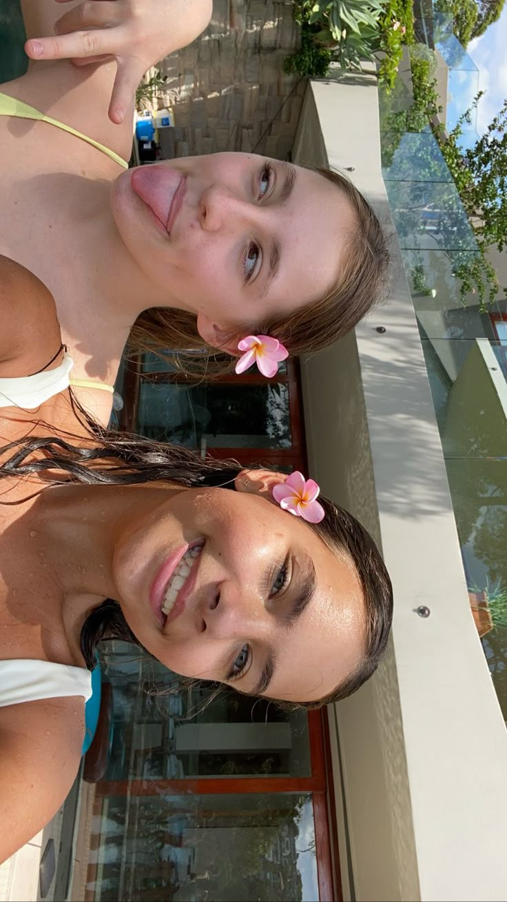 two young women standing next to each other in front of a pool with flowers on their hair