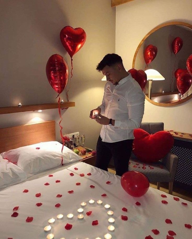 a man standing in front of a bed with red heart shaped balloons on the bed