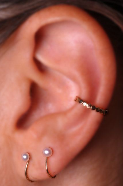 a close up of a person's ear with a gold nose ring and pearl beads