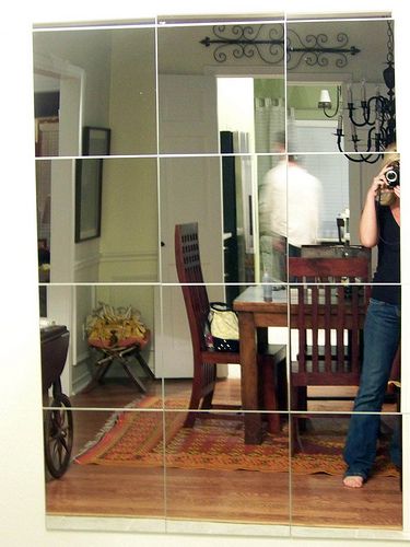 a woman taking a photo in front of a mirror with the reflection of a dining room table