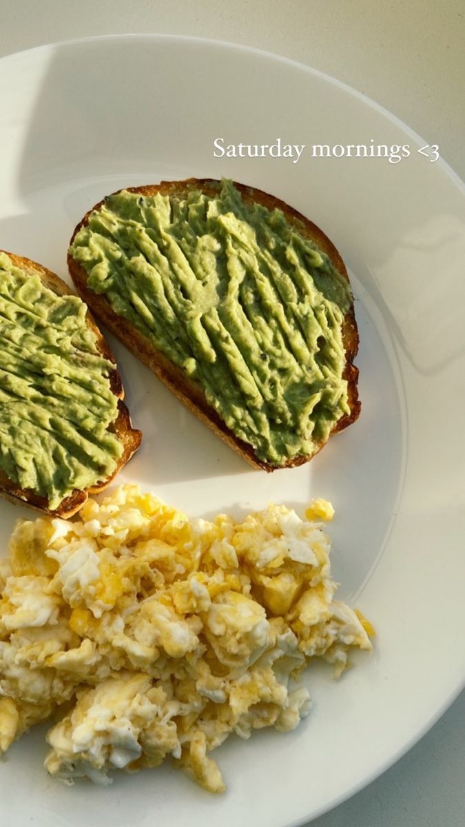 two pieces of toast with avocado and scrambled eggs on them sitting on a white plate