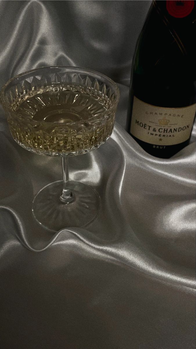 a wine glass sitting next to a bottle on top of a silver cloth covered table