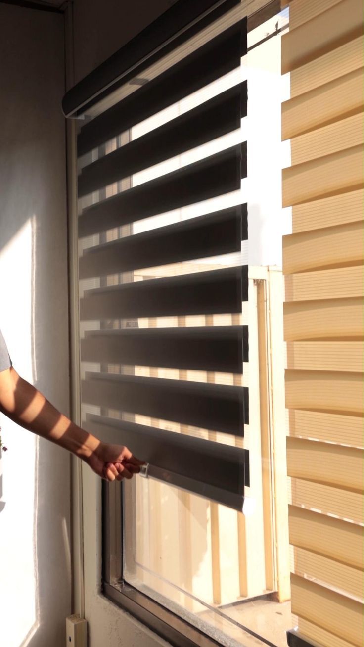 a woman standing next to a window with blinds on it