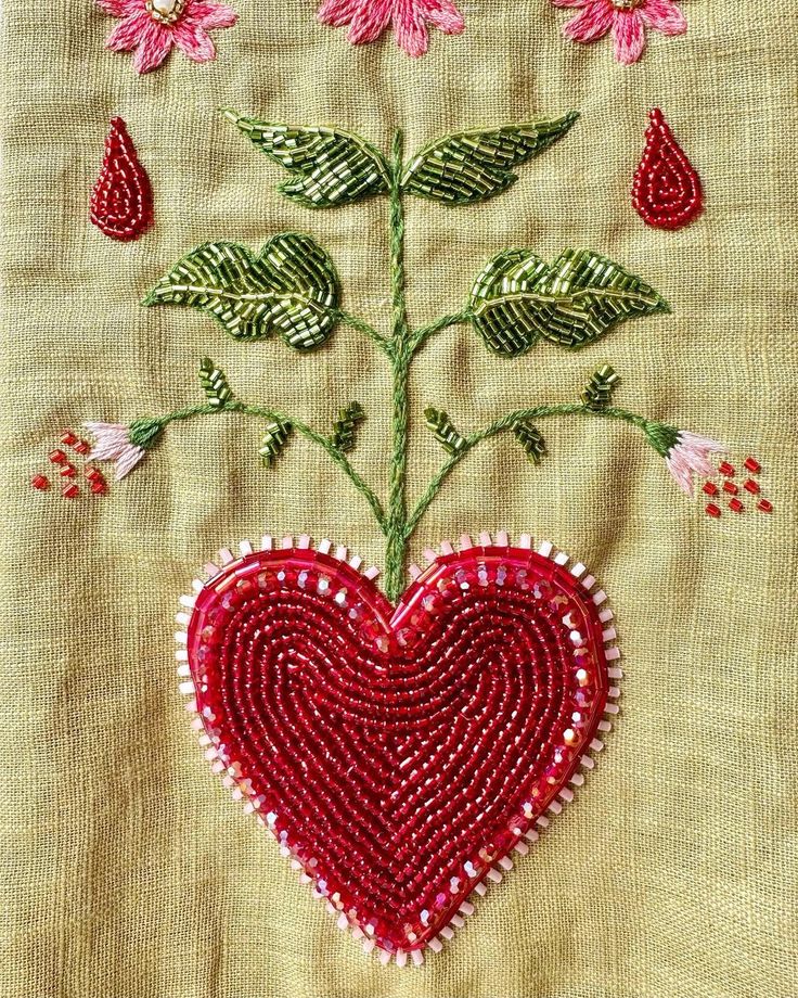 a red heart shaped beaded with flowers and leaves on a piece of cloth that has been stitched together