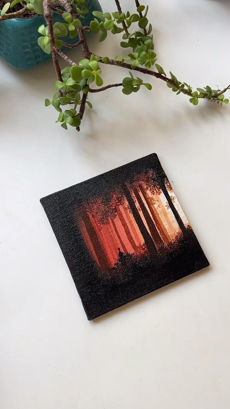 a plant is sitting on a table next to a card with an image of trees