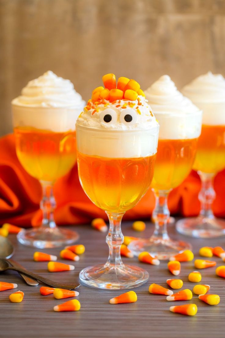 three glasses filled with orange liquid and candy corn on top of each glass, sitting on a table