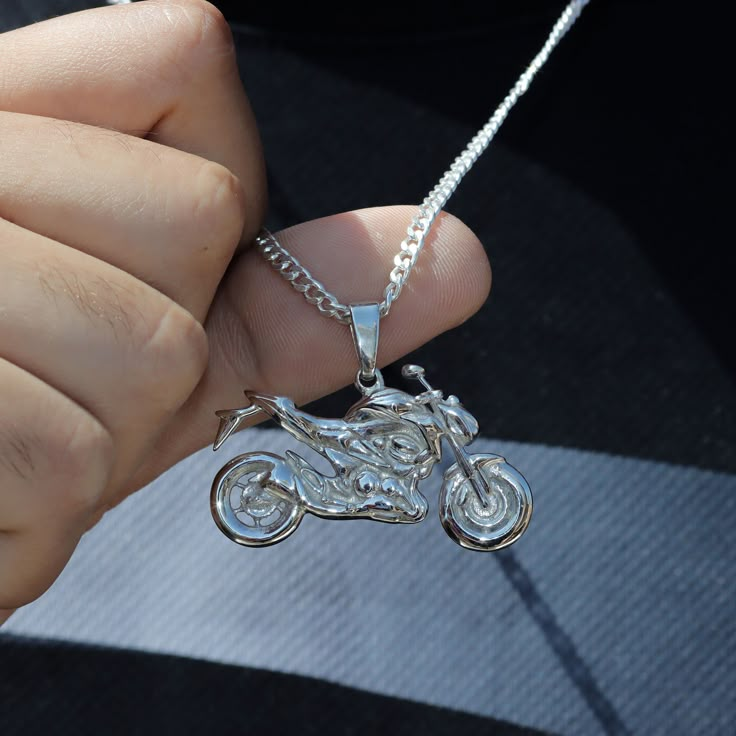 a person holding a silver necklace with a motorcycle on it