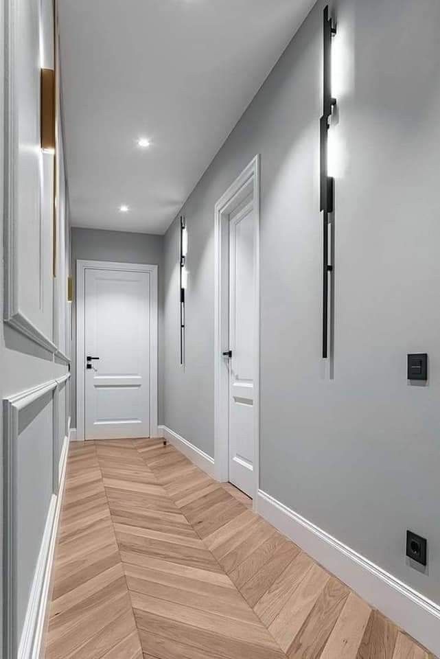 an empty hallway with white walls and wooden floors is lit by recessed lights on either side