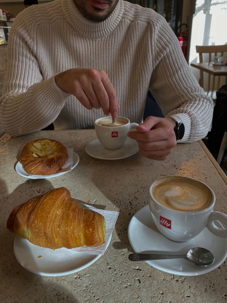 a man sitting at a table with coffee and croissants