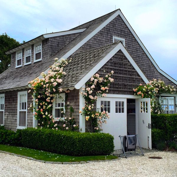 a house with roses on the front and side of it's roof, next to a gravel driveway