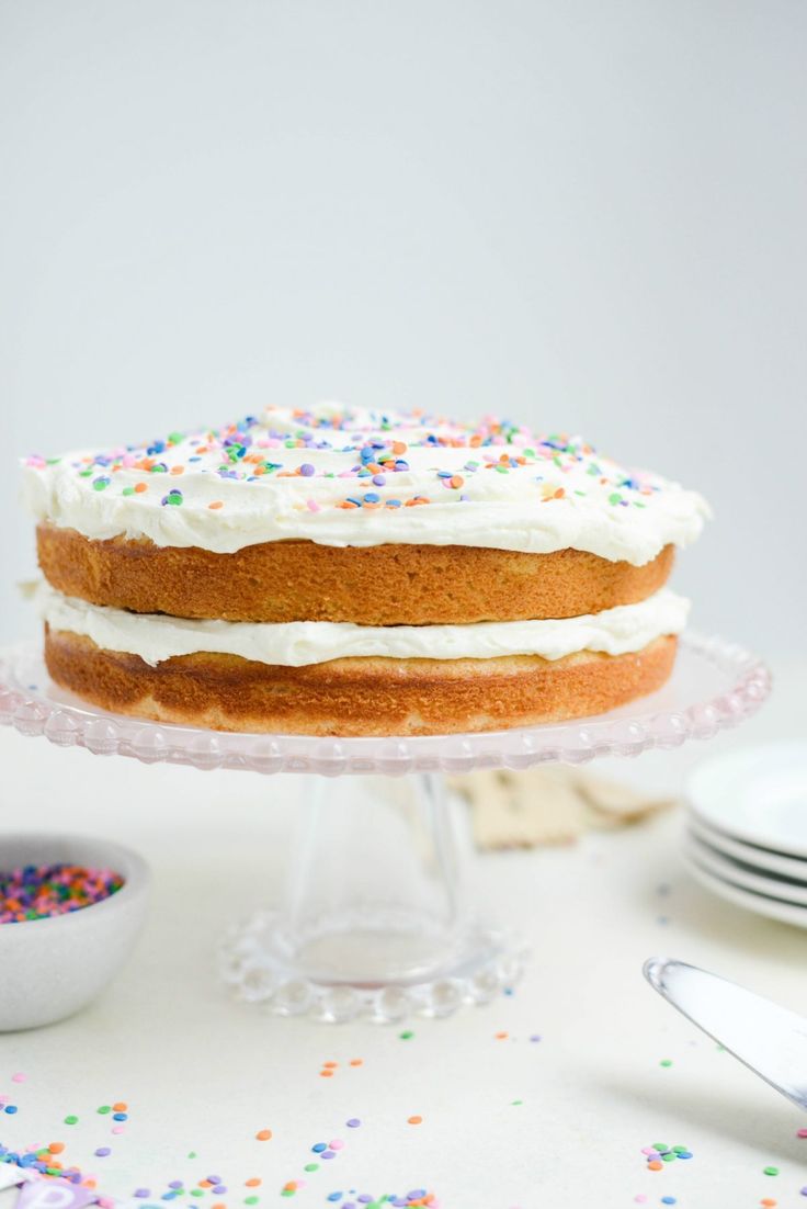 a cake with white frosting and sprinkles sitting on a glass stand