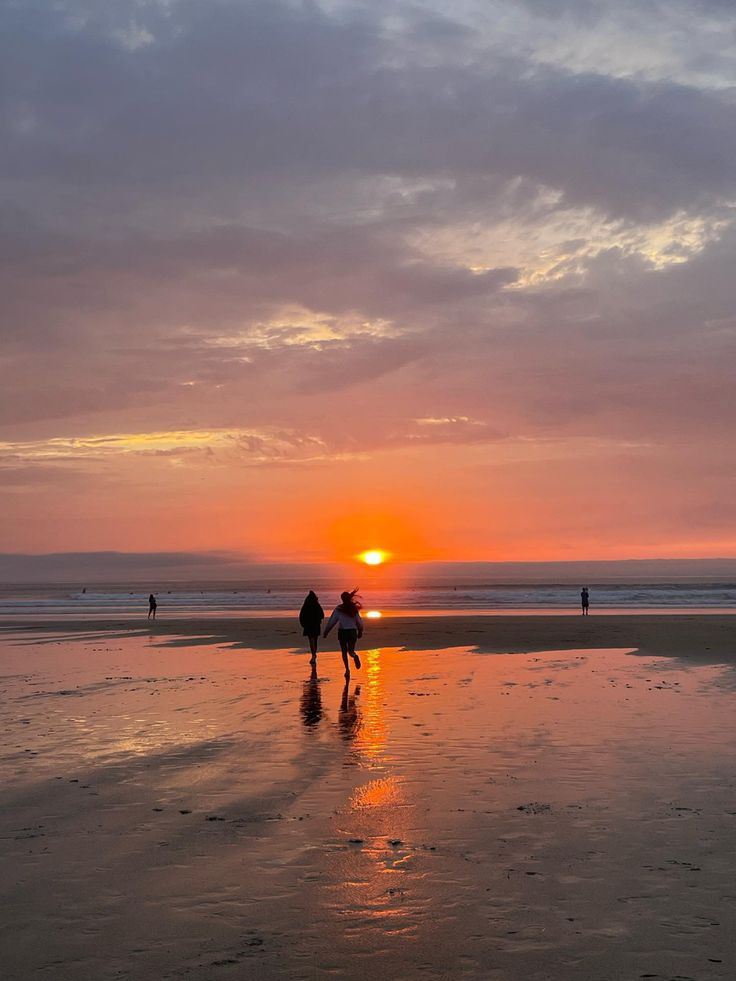 two people walking on the beach at sunset