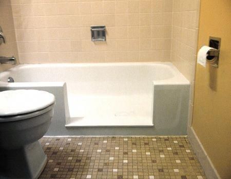 a white toilet sitting next to a bath tub in a bathroom with tiled flooring