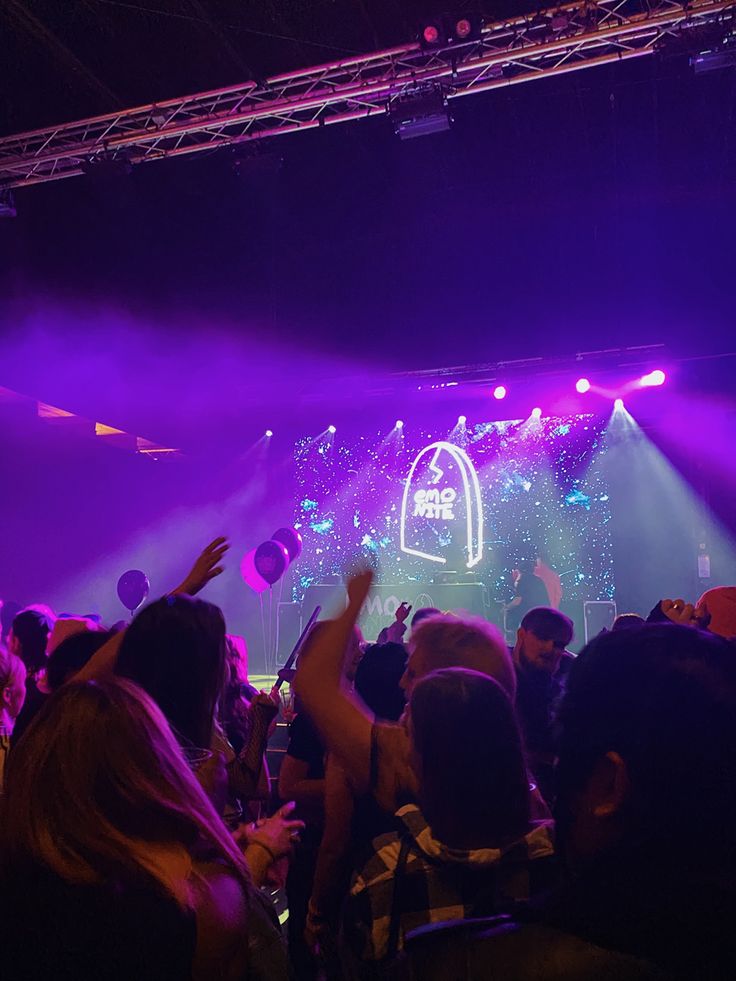 a large group of people at a concert with their hands in the air and lights on