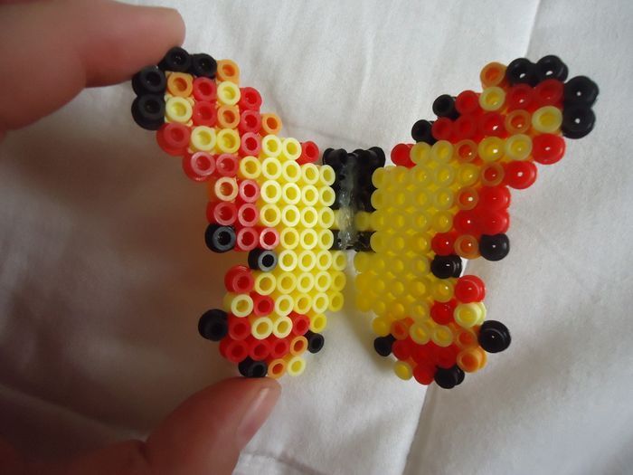 a hand holding a beaded butterfly on top of a white sheet with other beads