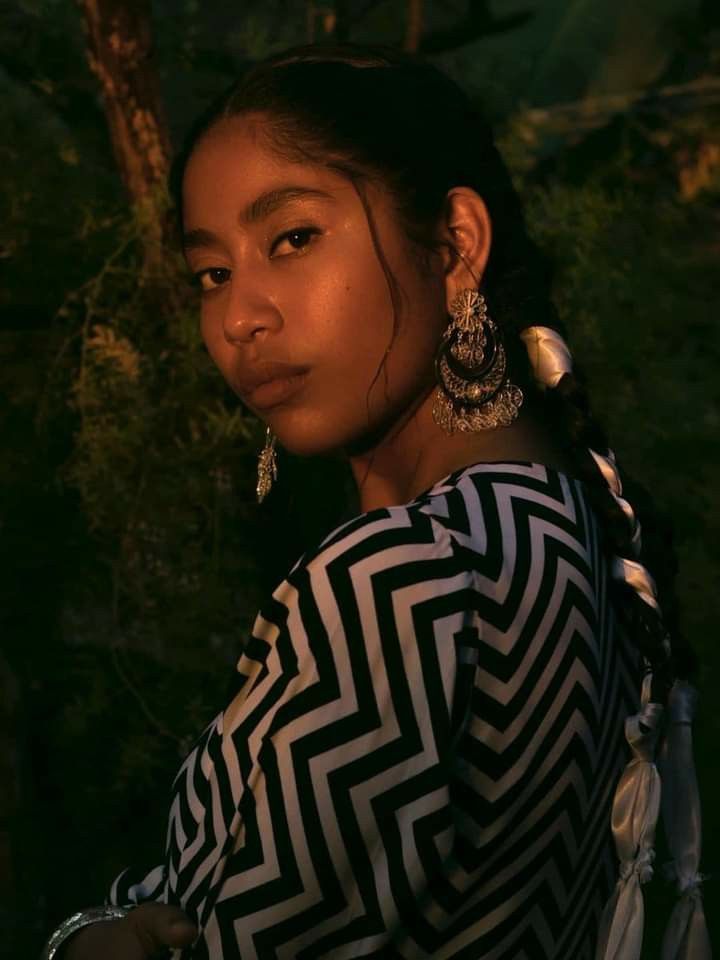 a woman in a black and white dress standing next to a tree with large earrings on her head