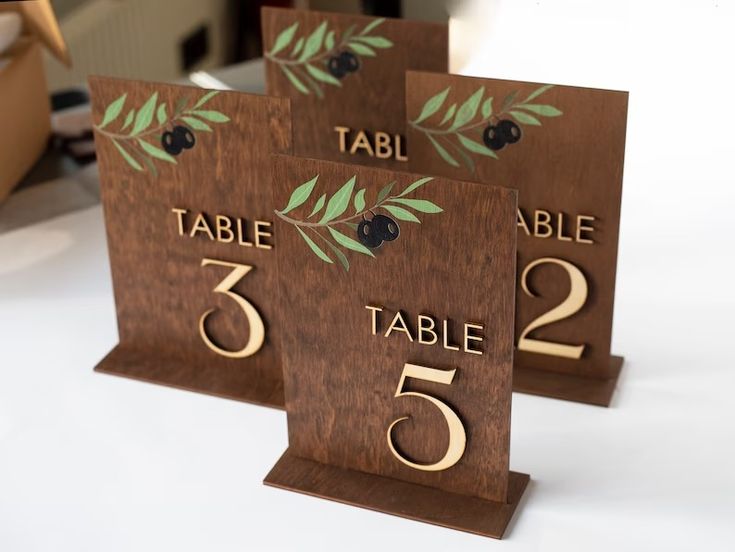 three wooden table numbers with olive leaves on them