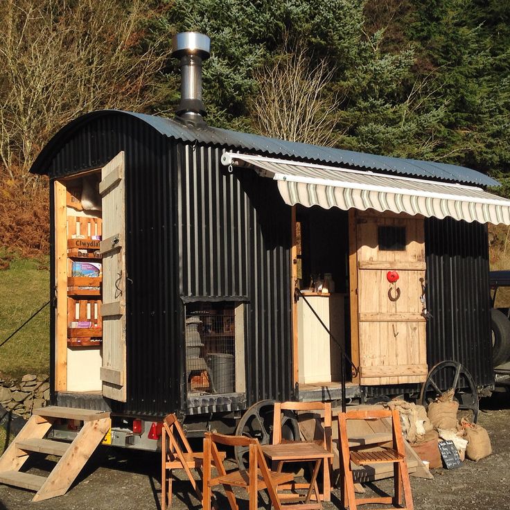 a small black shed with wooden chairs around it