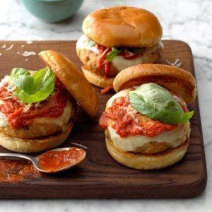 three mini burgers on a wooden tray with sauce