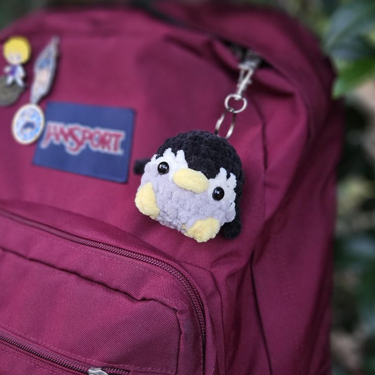 a purple backpack with a small stuffed penguin on it's back pocket and some badges attached to the front