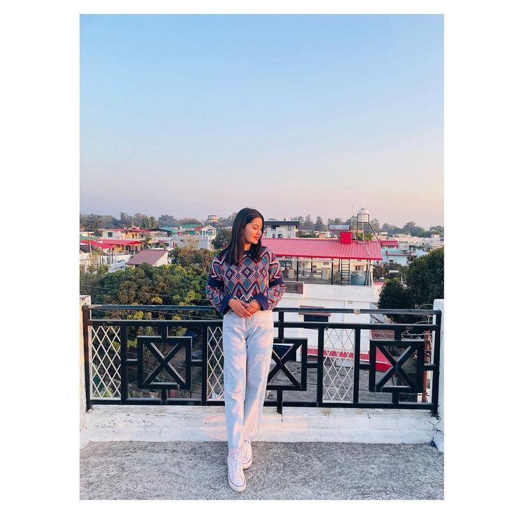 a woman standing on top of a balcony next to a railing with buildings in the background