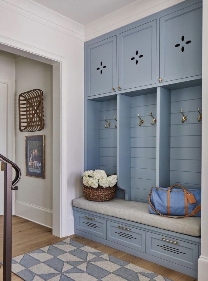 an entryway with blue cabinets and flowers in a basket on the bench next to it