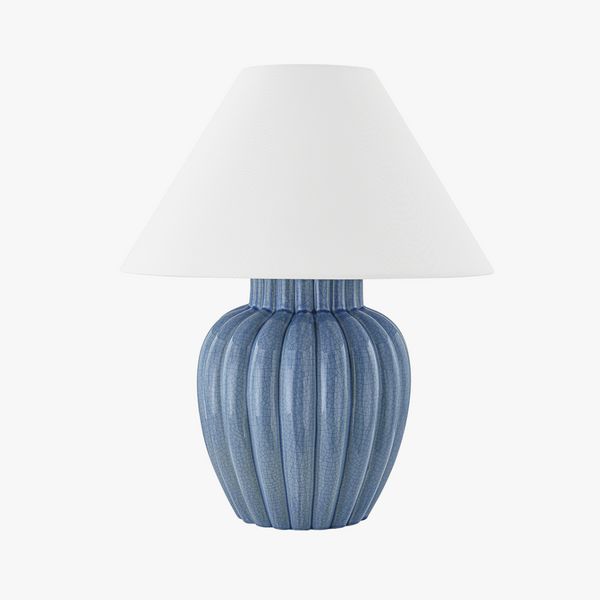 a blue ceramic lamp with a white shade on the top and bottom, against a white background