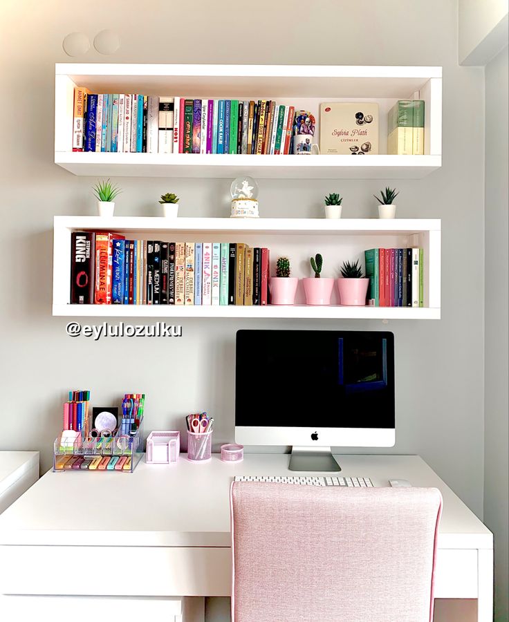 a desk with a computer, bookshelf and pink chair in front of it