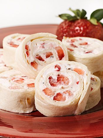 there are several rolls on the plate with strawberries next to it and a strawberry in the background