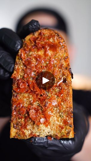 a person wearing black gloves holding a piece of pizza in their hand with a video playing on it