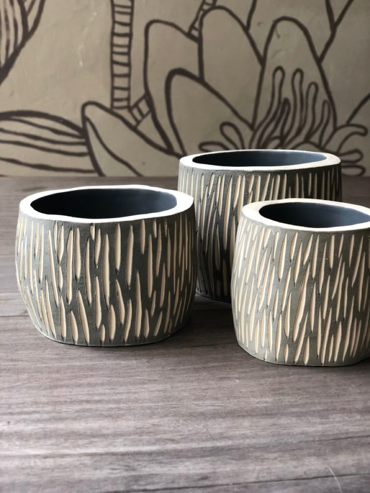 three black and white vases sitting on top of a wooden table next to a wall