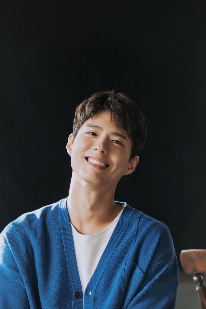 a young man is smiling while sitting in front of a black background and wearing a blue cardigan