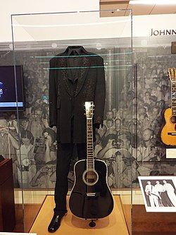 an acoustic guitar and suit on display in a glass case with the image of elvis presley