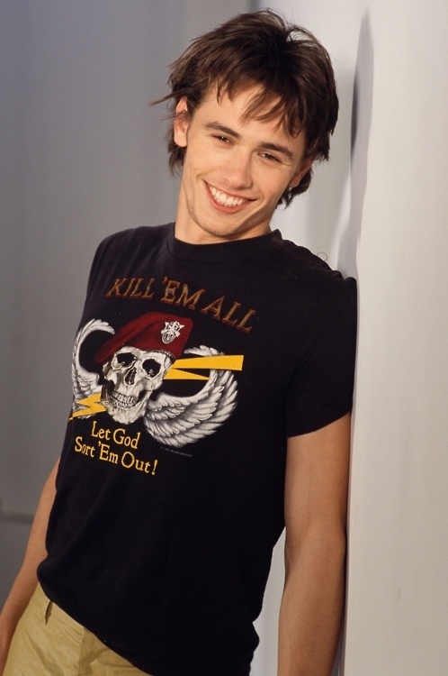 a young man leaning against a wall wearing a t - shirt that says kill em all