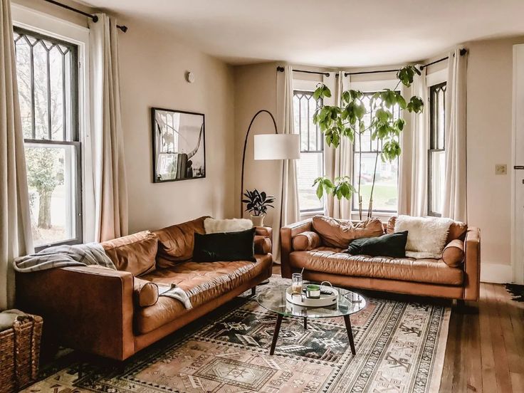 a living room with two couches and a rug on the floor in front of three windows