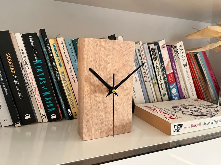 a wooden clock sitting on top of a book shelf next to a pile of books