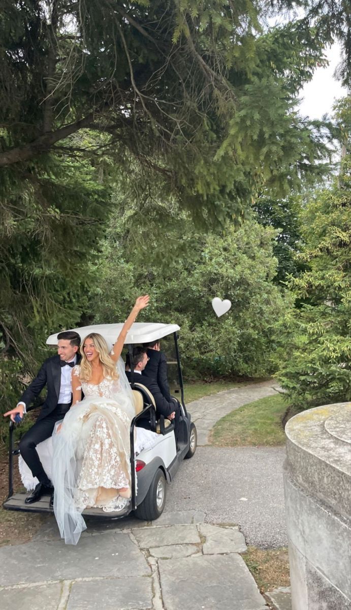 a bride and groom riding in a golf cart with their arms up to the sky