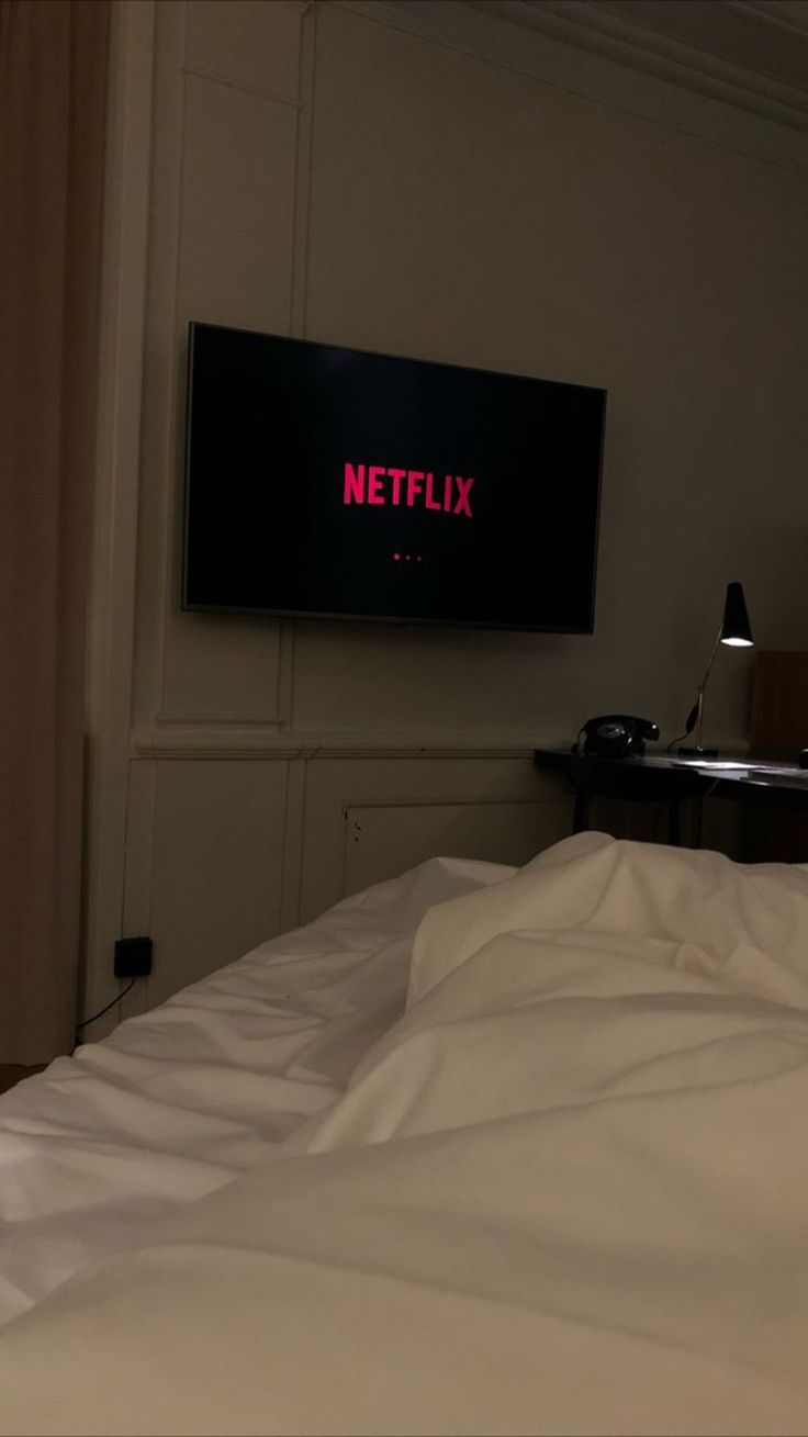 there is a television that is on the wall above a bed with white sheets and pillows