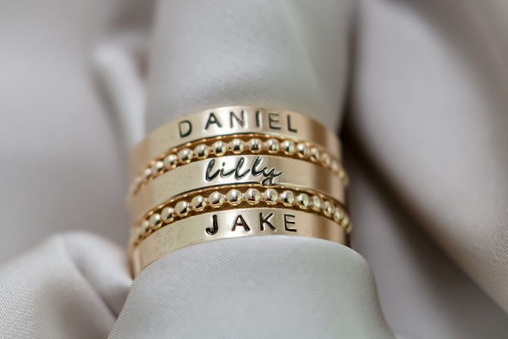 Create your own beautiful set of name rings to show off the people closest to your heart! So simply pretty! Our 3mm high quality 14k Gold-Filled band rings fit one date, name or word in your choice of font. Our rings stack beautifully together, so purchase up to 3 name band rings total for one finger. Please keep the total characters per ring to around 20 max. Up to 3 name ring bands with two spacers will fit on one finger, and we recommend sizing to the next whole size up if you are stacking 3 rings. Please read the sizing details first in the DETAILS section below. D E T A I L S 14k Gold Filled Name Band Rings: Whole US Sizes: 4 - 10 Option to add spacer rings Lowercase tiny script font or UPPERCASE Arial Choose natural or darkened lettering Fit one name, date or word per ring Stamped by Trendy Rings For Women, Stackable Rings For Each Child, Spacer Rings, Rings Stack, Ring Bands, One Finger, Ring Spacer, Baby Rings, Name Ring