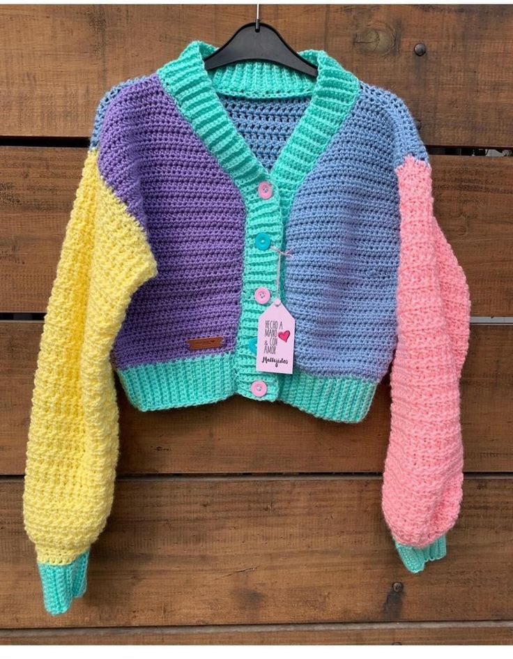 a colorful knitted sweater hanging on a wooden wall next to a coat hanger