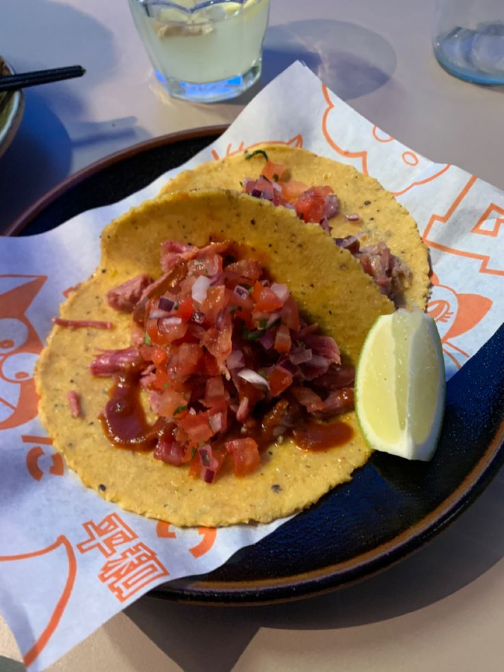 two tacos on a plate with a lemon wedge