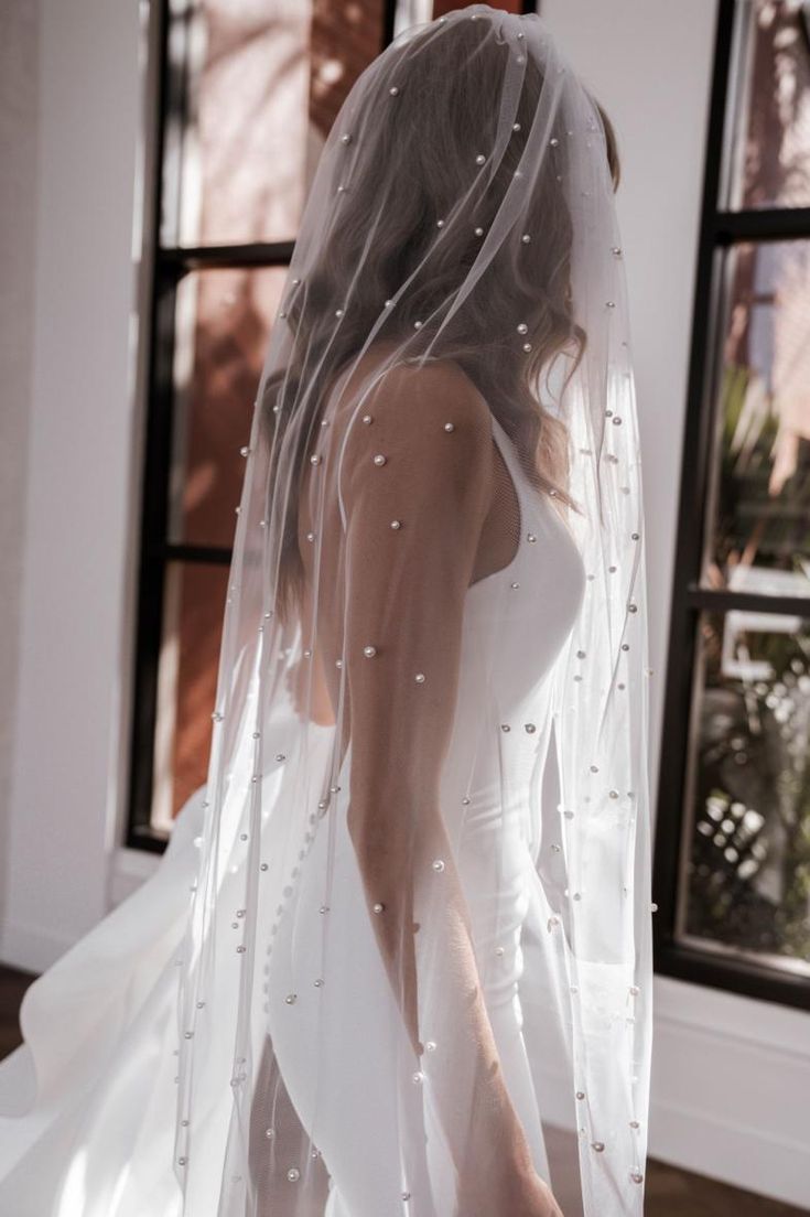 a woman wearing a wedding veil and dress in front of a window with her hands on her hips