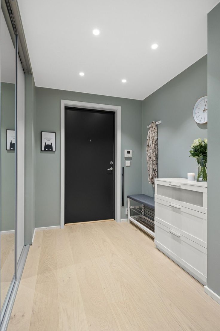 an empty room with a black door and white drawers on the floor, next to a bench