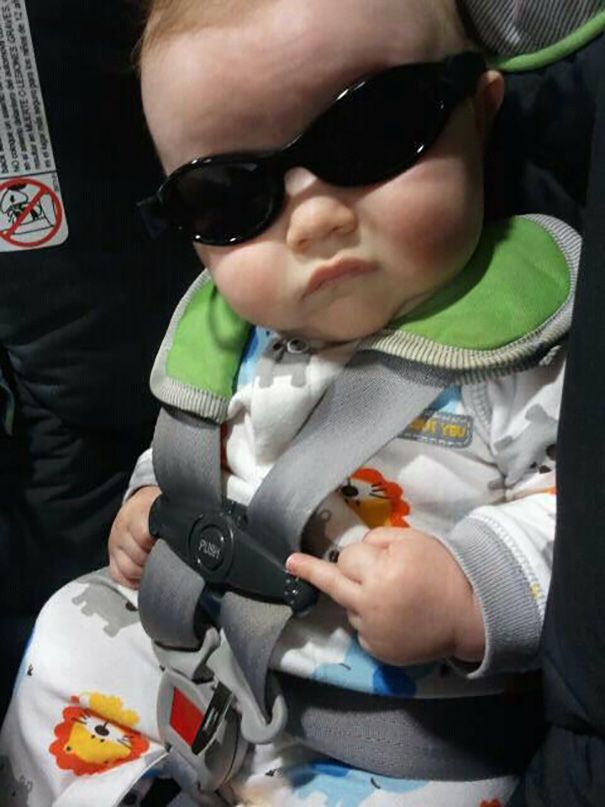 a baby wearing sunglasses sitting in a car seat with his head turned to the side