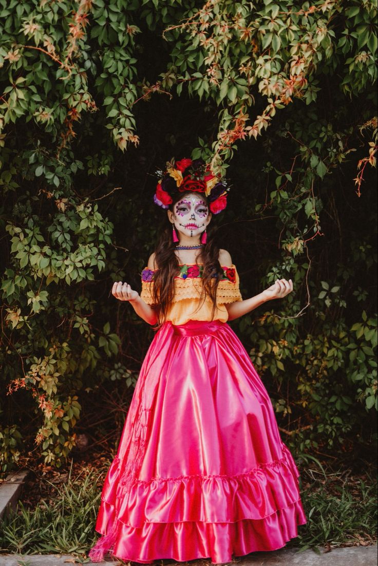 a woman in a pink dress with flowers on her head and makeup painted to look like a skeleton