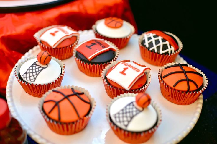 cupcakes decorated with sports themed icing are on a white plate next to red and black napkins